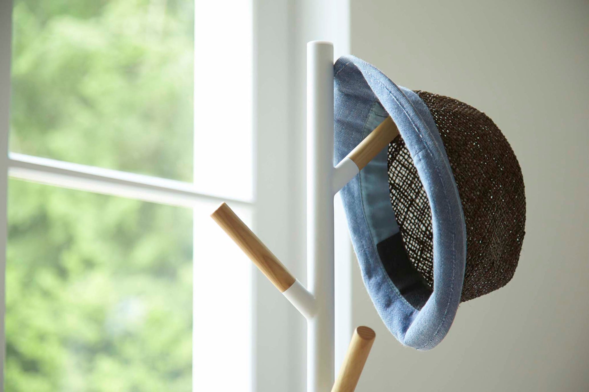 White Coat Rack from Yamazaki Home holding a light summer hat in a breezy entryway.