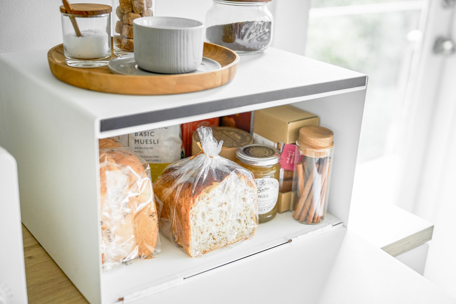White steel bread box from Yamazaki Home holding various pastries, breads, and spreads. Other ingredients are held in a dish on top of the box. 