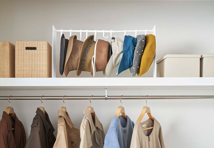 Organized closet featuring a rod of hanging clothes and an upper-level shelf with the Yamazaki Home Hat hanging organizer and several storage boxes. Image shows off the joy of an organized closet. 