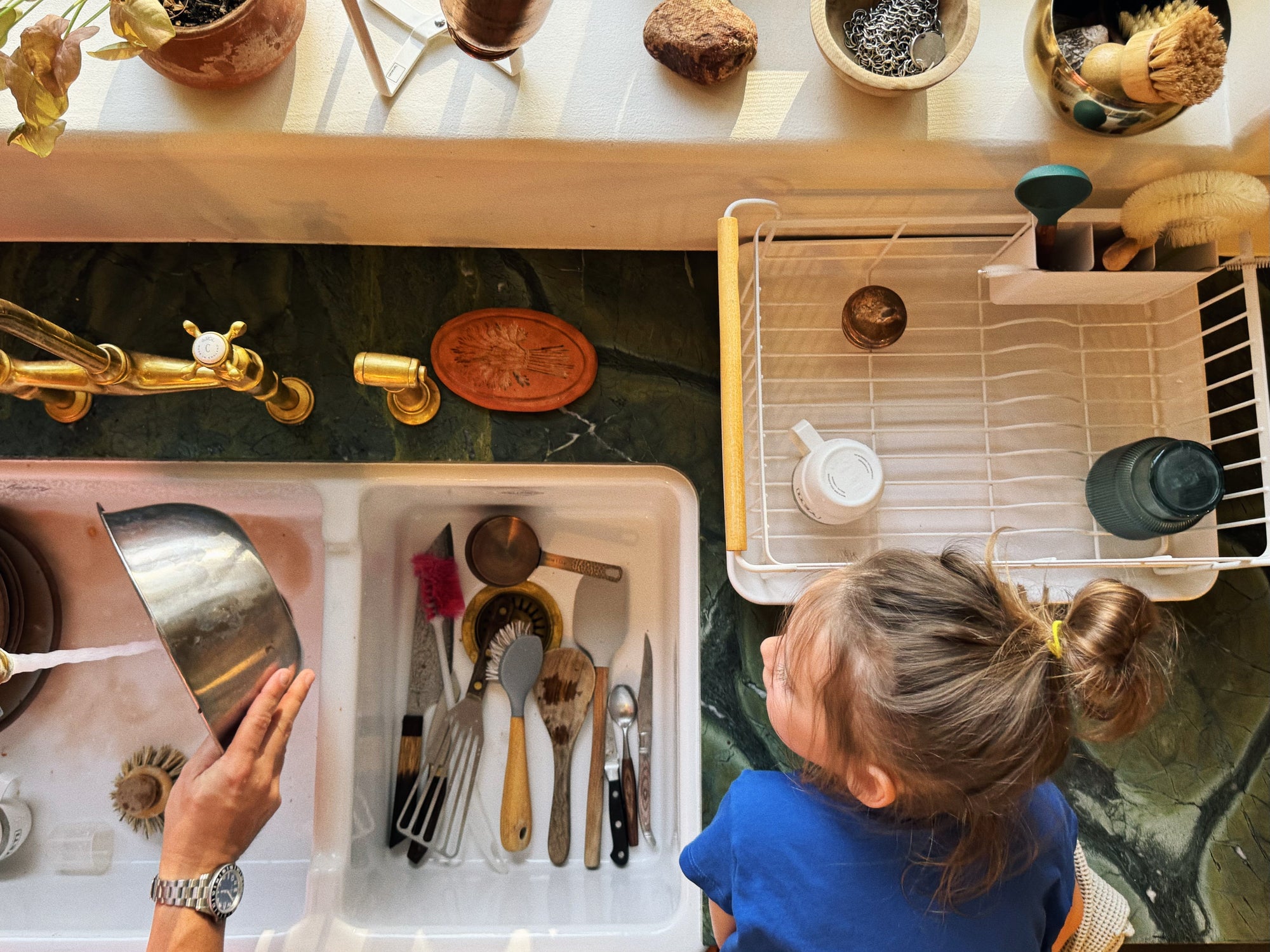 Aerial view of father and child doing dishes at the sink. The Yamazaki Home dish rack sits in the right corner, used to dry dishes. The daughter helps her father rinse and dry dishes. 