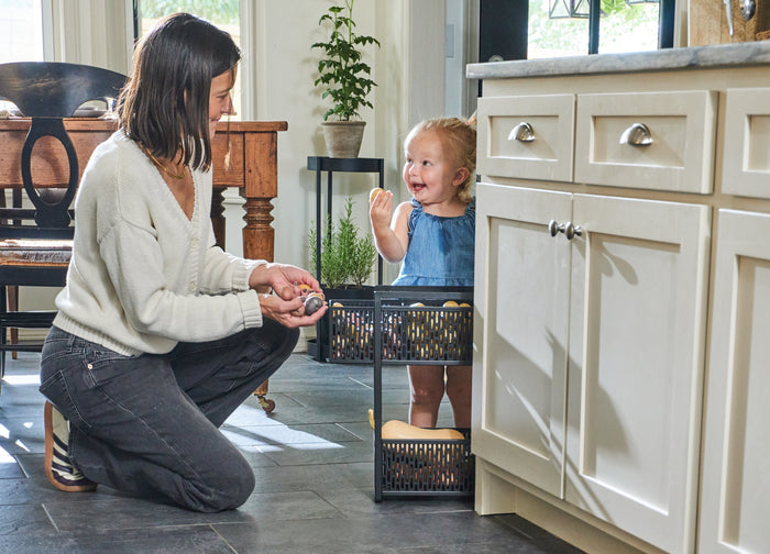 Ashley Jenke and her daughter smile at each other in a charming kitchen over the Tower Two-tier cabinet storage basket from Yamazaki Home.