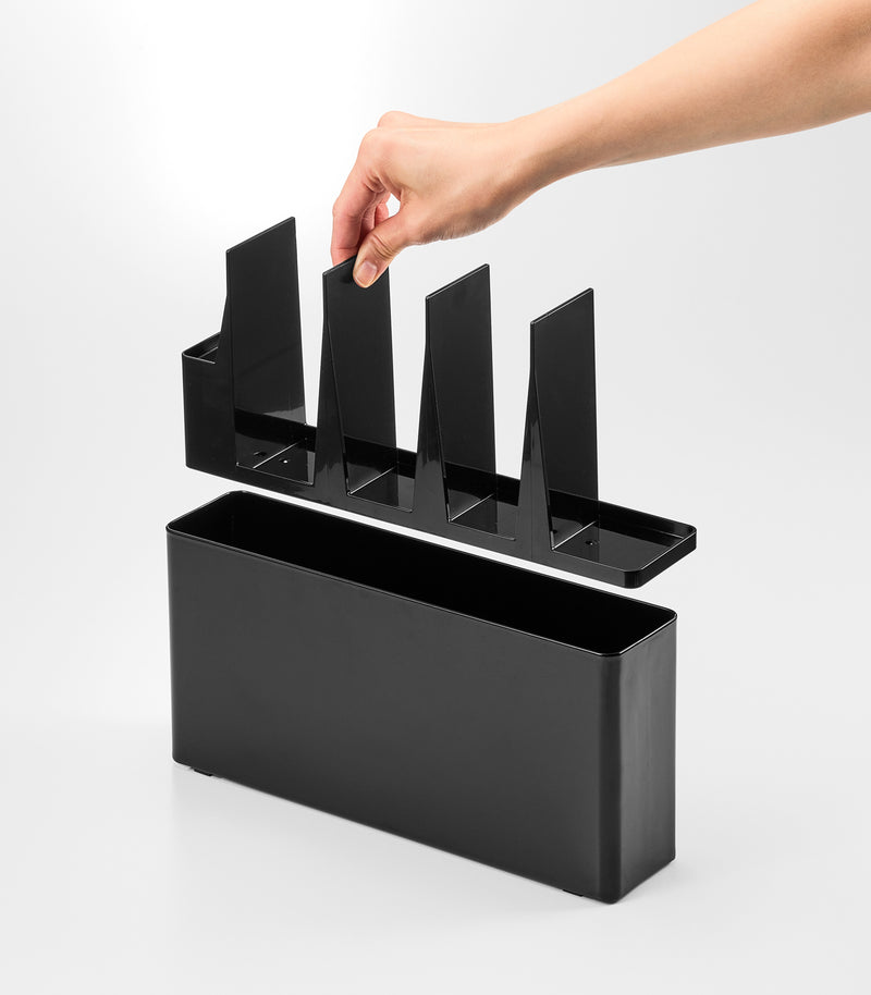 Black Utensil & Thin Cutting Board Holder by Yamazaki Home with a hand placing a cutting board into one of its slots.