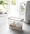 A Yamazaki Rolling Wire Basket holding laundry near a laundry machine.