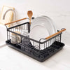 Black steel dish drying rack with wood handles on a drying tray in a modern kitchen with marble countertop near a sink from Yamazaki Home.