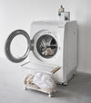 A Yamazaki Rolling Wire Basket in front of an open laundry machine.
