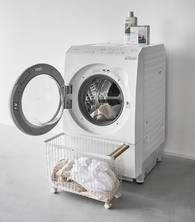 A Yamazaki Rolling Wire Basket in front of an open laundry machine.