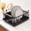 Black steel dish drying rack with wood handles on a drying tray from Yamazaki Home next to a sink in a modern kitchen with marble countertop.