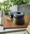 Black Yamazaki Mosquito Repellant Coil Holder and Storage Case lit on a table outside beside a candle