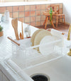 White Over-the-Sink Expandable Dish Drying Rack holding dishware and silverware in kitchen by Yamazaki Home.