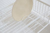 Close up view of white Over-the-Sink Expandable Dish Drying Rack holding plate in kitchen by Yamazaki Home.