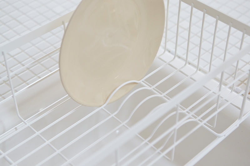 Close up view of white Over-the-Sink Expandable Dish Drying Rack holding plate in kitchen by Yamazaki Home.