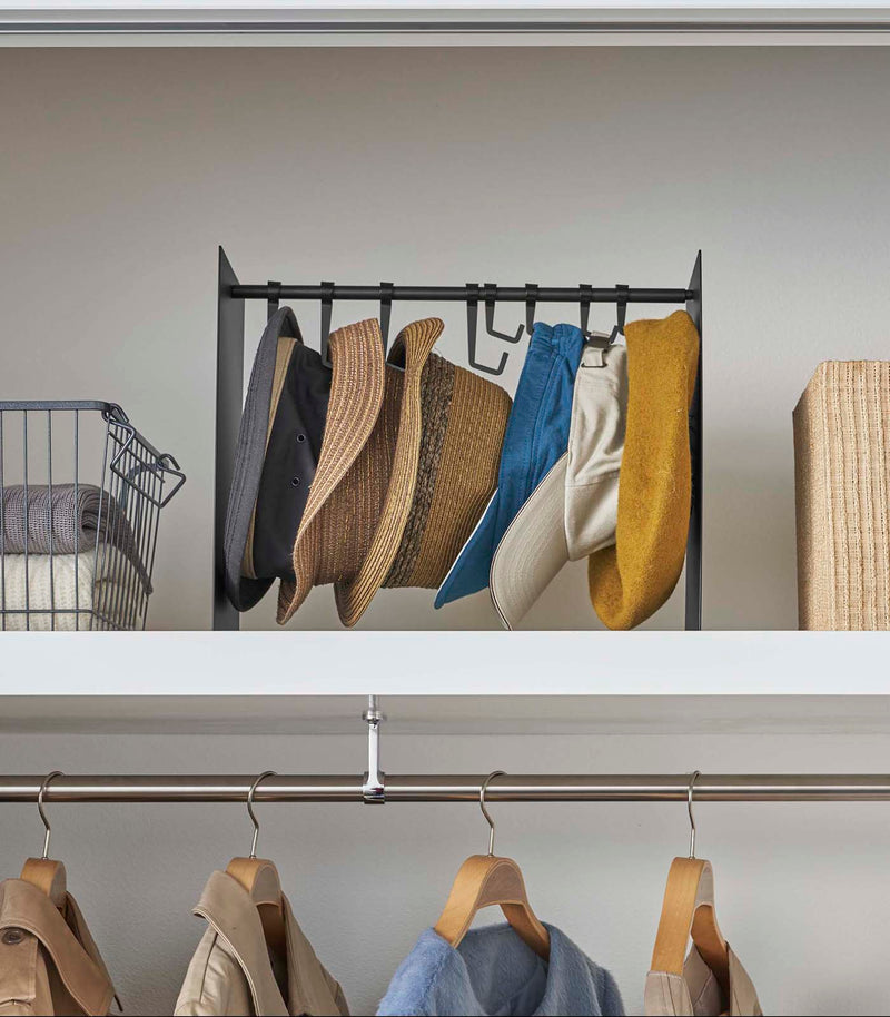 Frontal view of shortened black Yamazaki Home hat rack hanging a variety of hats in a closet