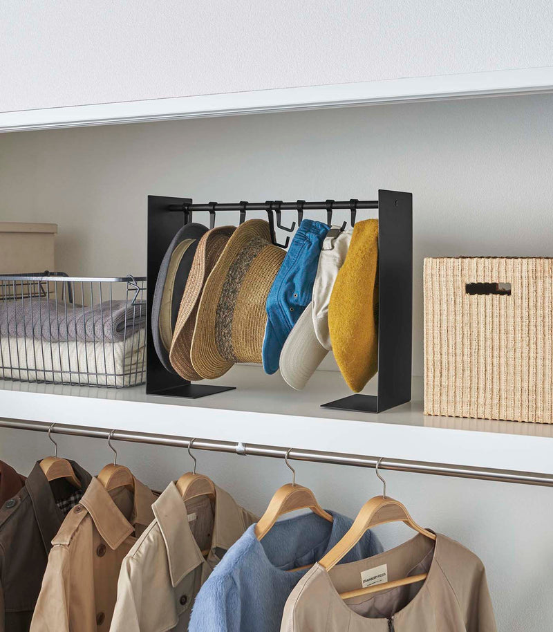Shortened black Yamazaki Home hat rack hanging a variety of hats in a closet