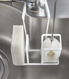 Close up of white Steel Yamazaki Home Faucet-Hanging Sponge & Brush Holder storing a brush and a sponge