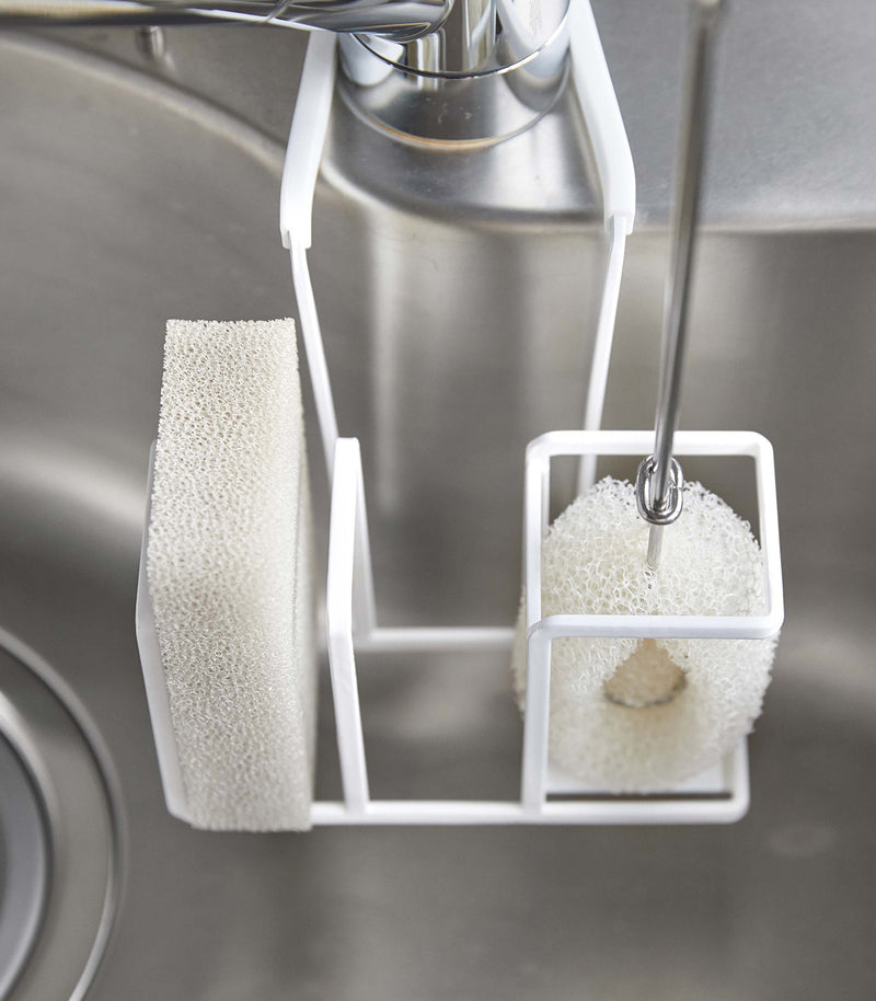 Close up of white Steel Yamazaki Home Faucet-Hanging Sponge & Brush Holder storing a brush and a sponge