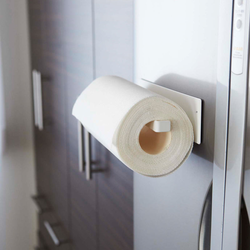 Side view of Yamazaki Home's Magnet Paper Towel Holder seen attached to a refrigerator door with a regular-sized roll of paper towels hanging on the arm.