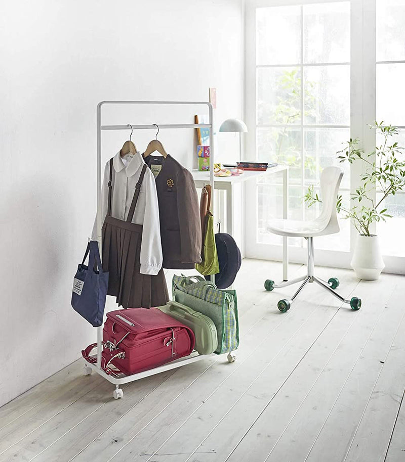 White Rolling Coat Rack holding school clothes, accessories and bags by Yamazaki Home.