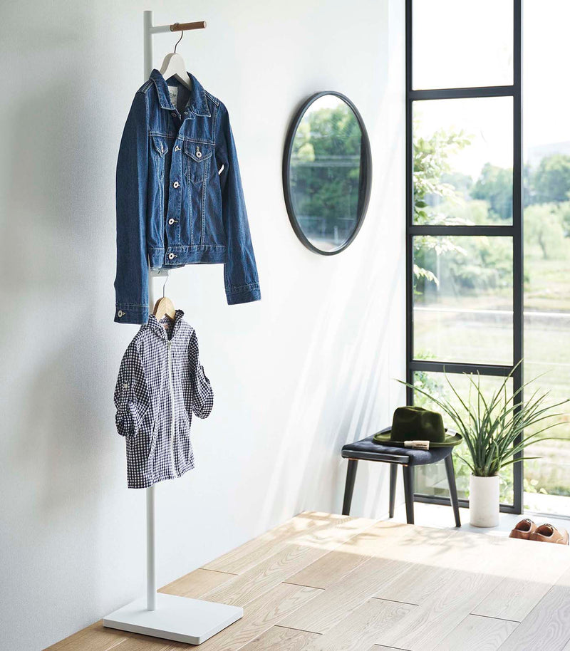 White Yamazaki Coat Rack placed in an entryway with a jacket and a child's shirt hanging on it