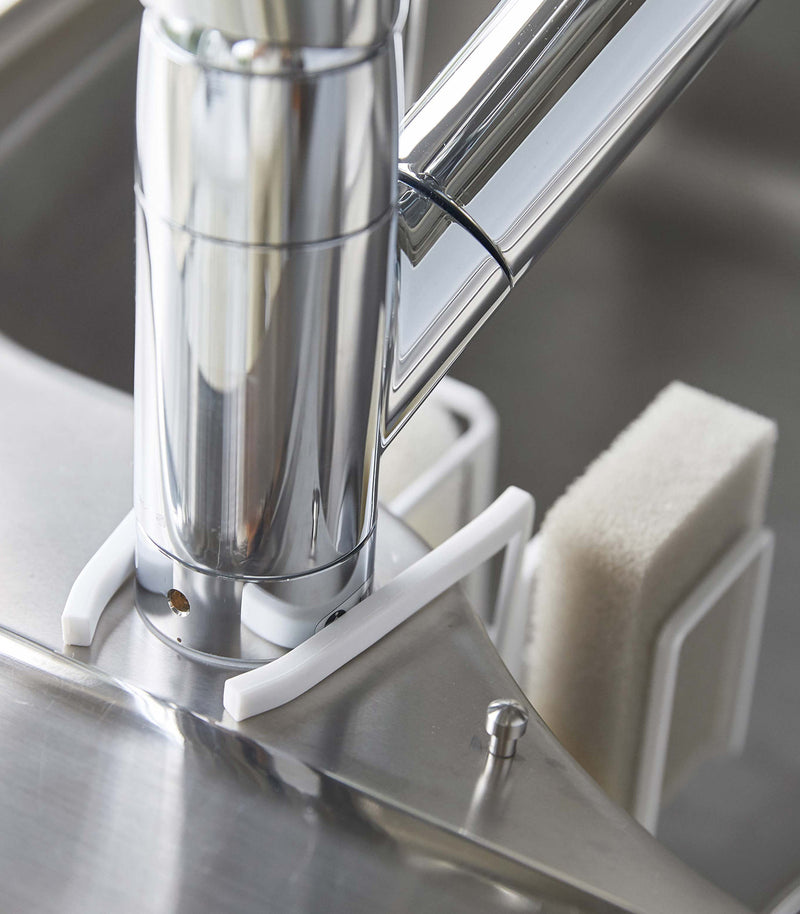 Close up of back of white Steel Yamazaki Home Faucet-Hanging Sponge & Brush Holder attached to a faucet