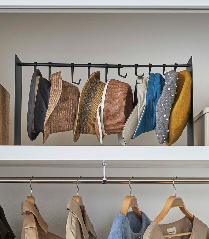 Frontal view of black Yamazaki Home hat rack hanging a variety of hats in a closet