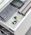 Two small stackable clear organizers are placed in a kitchen drawer, organizing small items like strings and tiny sauce bottles