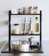Front view of Yamazaki Home Two-Tier Countertop Rack holding spices and oils.