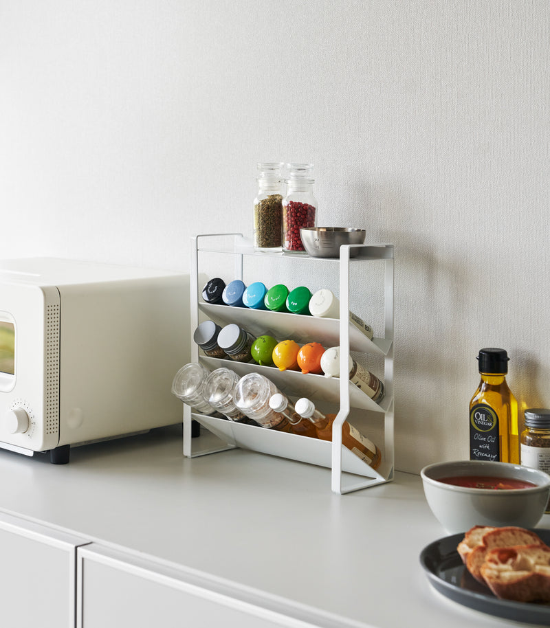 White Four-Tier Slim Spice Rack by Yamazaki Home in a well-lit kitchen, equipped with a variety of spices and essentials.
