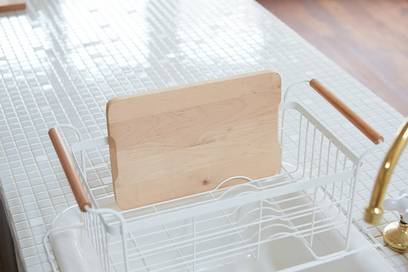 White Over-the-Sink Expandable Dish Drying Rack holding cutting board in kitchen by Yamazaki Home.
