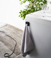 Black Yamazaki Home Traceless Adhesive Towel Holder attached to a washing machine with a towel inserted