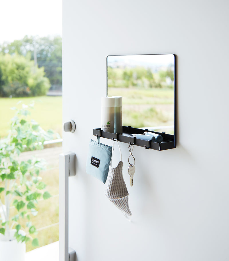 A black Yamazaki Magnetic Mirror With Storage Rack attached to a door with a hanging bag, mask, and key.