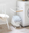 Rolling Wire Basket holding clothes in laundry room by Yamazaki Home.