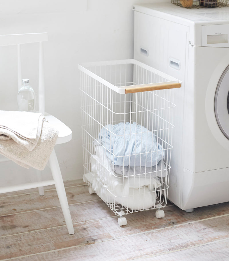 Rolling Wire Basket holding clothes in laundry room by Yamazaki Home.