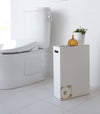 Side view of white Toilet Paper Stocker displaying phone and plant in bathroom by Yamazaki Home.
