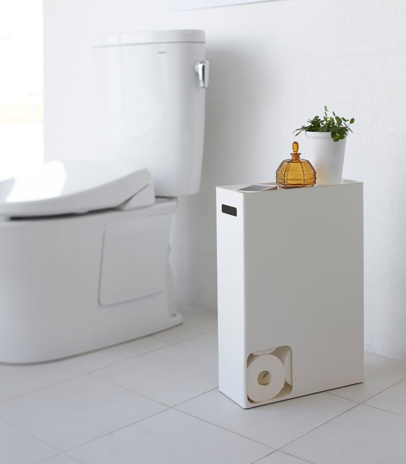Side view of white Toilet Paper Stocker displaying phone and plant in bathroom by Yamazaki Home.
