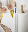 Close up view of white Paper Towel Holder holding paper towel on kitchen shelf by Yamazaki Home.