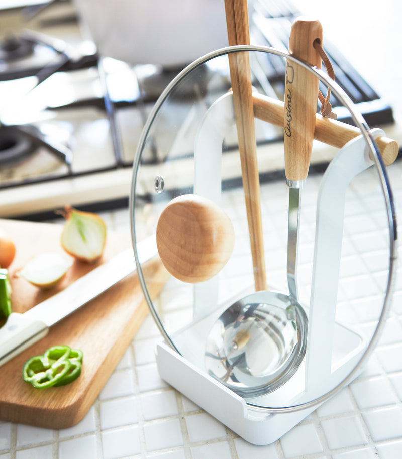 White Lid & Ladle Stand holding tongs, ladle, and pot cover on kitchen counter by Yamazaki Home.