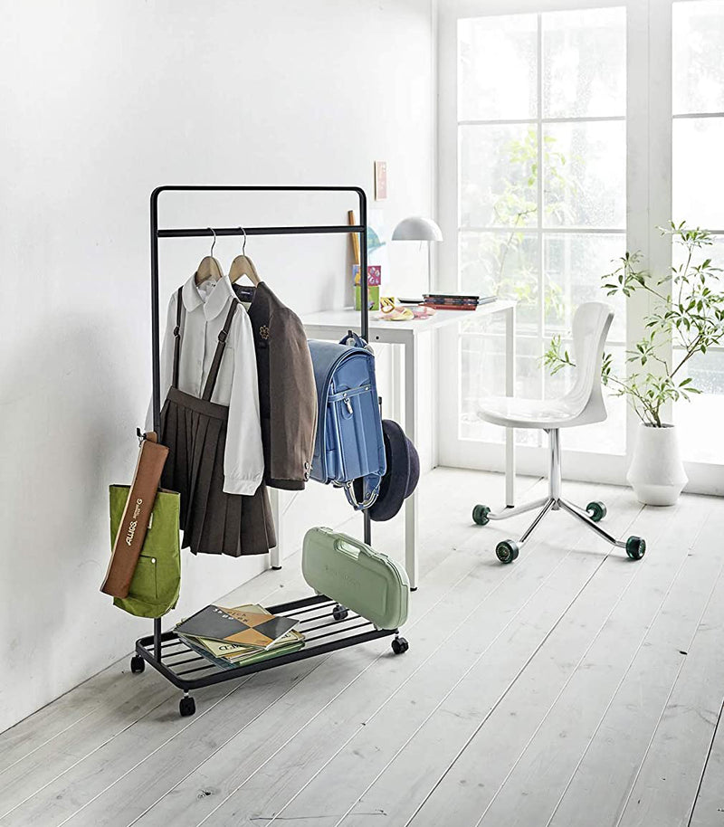 Black Rolling Coat Rack holding school uniform, backpack, hat, and school supplies by Yamazaki Home.