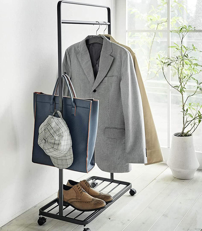 Black Rolling Coat Rack holding jackets, bag, hat, and shoes by Yamazaki Home.