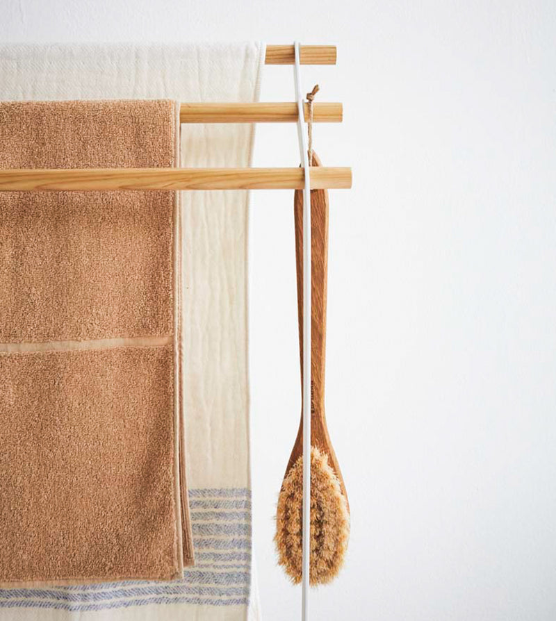 Front view of Bath Towel Rack holding towels and brush on white background by Yamazaki Home.