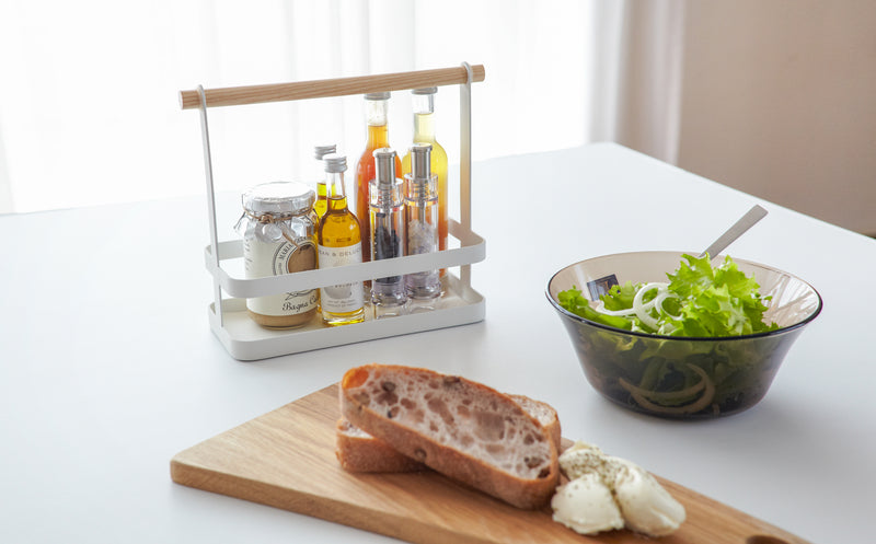 Front view of white Countertop Storage Caddy holding spices on kitchen table by Yamazaki Home.