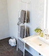 White Leaning Ladder Rack holding bath towels and hangers in bathroom by Yamazaki Home.