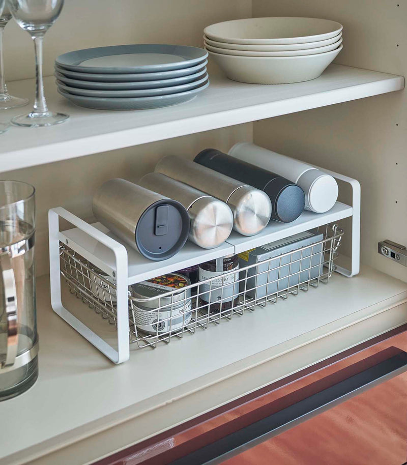 White Expandable Countertop Organizer expanded holding bottles in kitchen cabinet by Yamazaki Home.