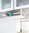 White Undershelf Organizer hanging from cabinet holding storage items and towels by Yamazaki Home.
