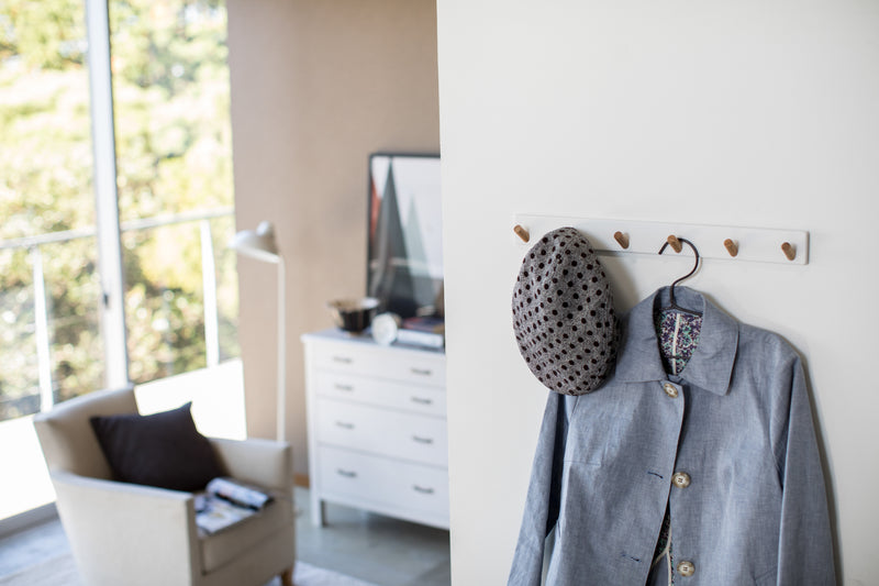 White Wall-Mounted Coat Hanger holding hat and jacket by Yamazaki Home.