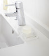 Clear Self-Draining Soap Tray holding soap on sink counter by Yamazaki Home.