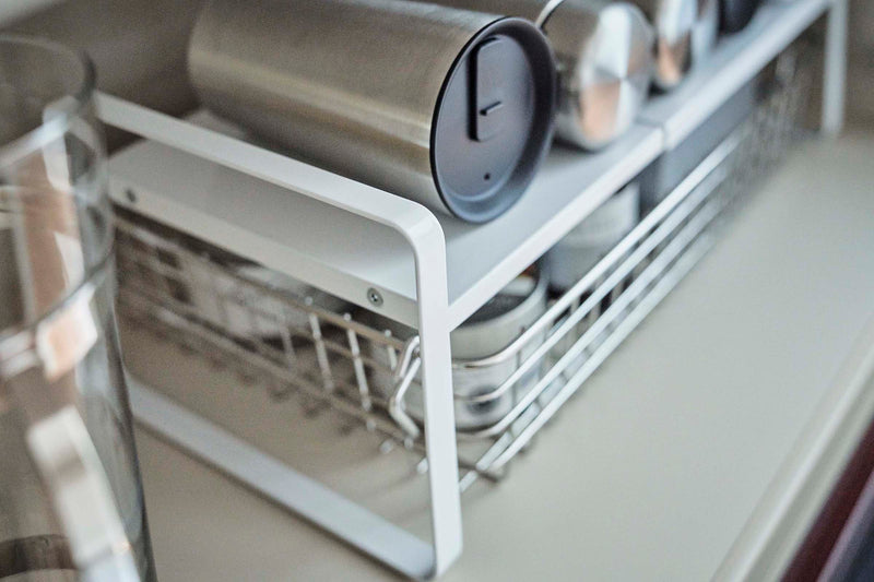 Close up view of white Expandable Countertop Organizer holding bottles in cabinet by Yamazaki Home.
