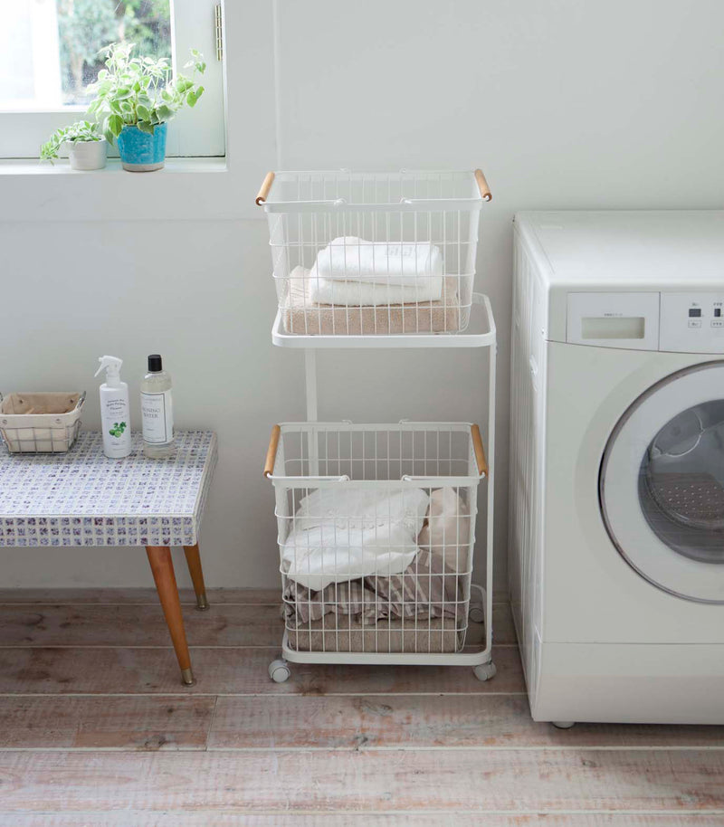 Front view of white Laundry Wagon and Basket holding clothes and towels in laundry room by Yamazaki Home.