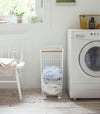 Side view of Rolling Wire Basket holding clothes in laundry room by Yamazaki Home.