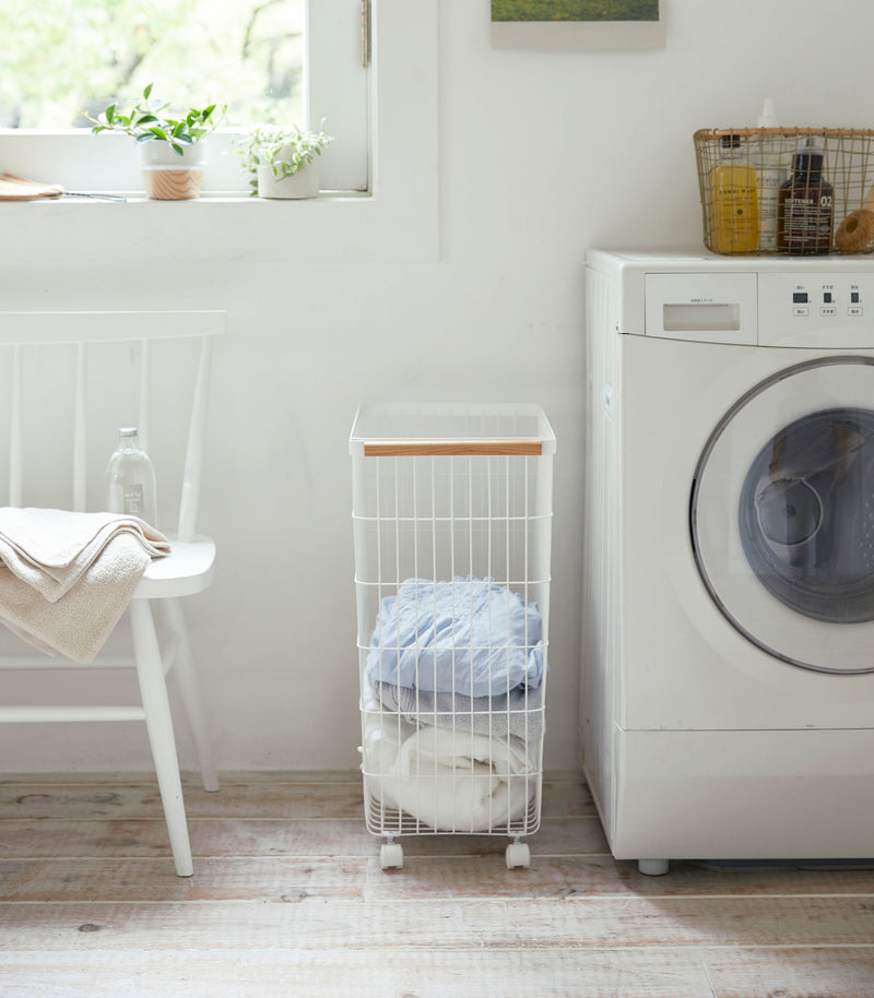 Side view of Rolling Wire Basket holding clothes in laundry room by Yamazaki Home.