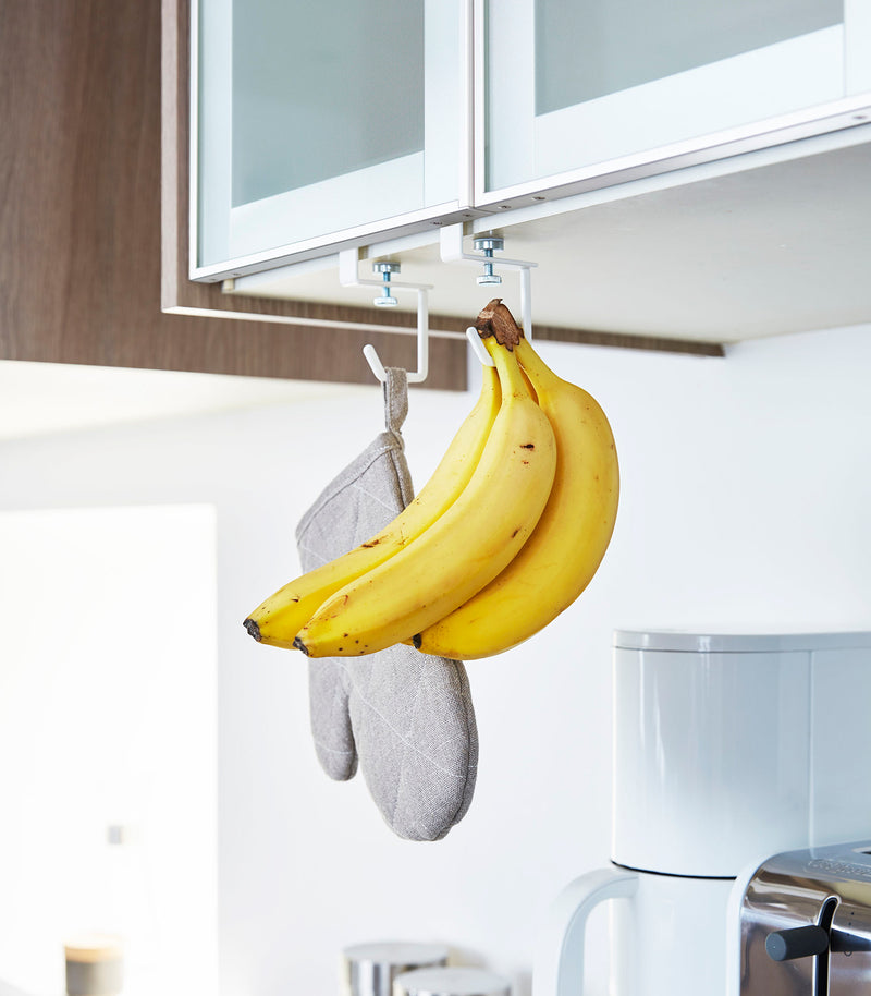 White Undershelf Hangers in kitchen holding oven mitt and bananas by Yamazaki Home.